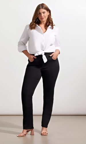 Woman in a white shirt tied at the waist and black pants, standing in front of a white background.