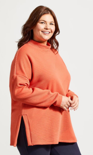 Woman in a coral-colored sweater smiles, with side slits, against a white background.