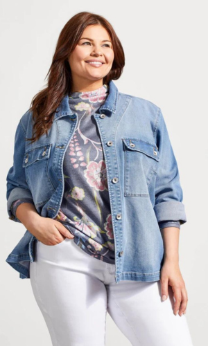Woman wearing a denim jacket, floral shirt, and white pants, smiling and looking to the side.
