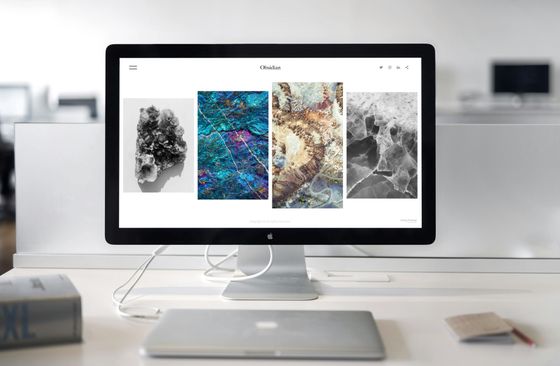 Desktop computer displaying a website with four abstract images: crystals, galaxy, rock, and stone, on a desk with a closed laptop.