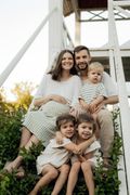 Family of five smiling, posing on outdoor white stairs. Two young girls hug, while other children and parents smile.