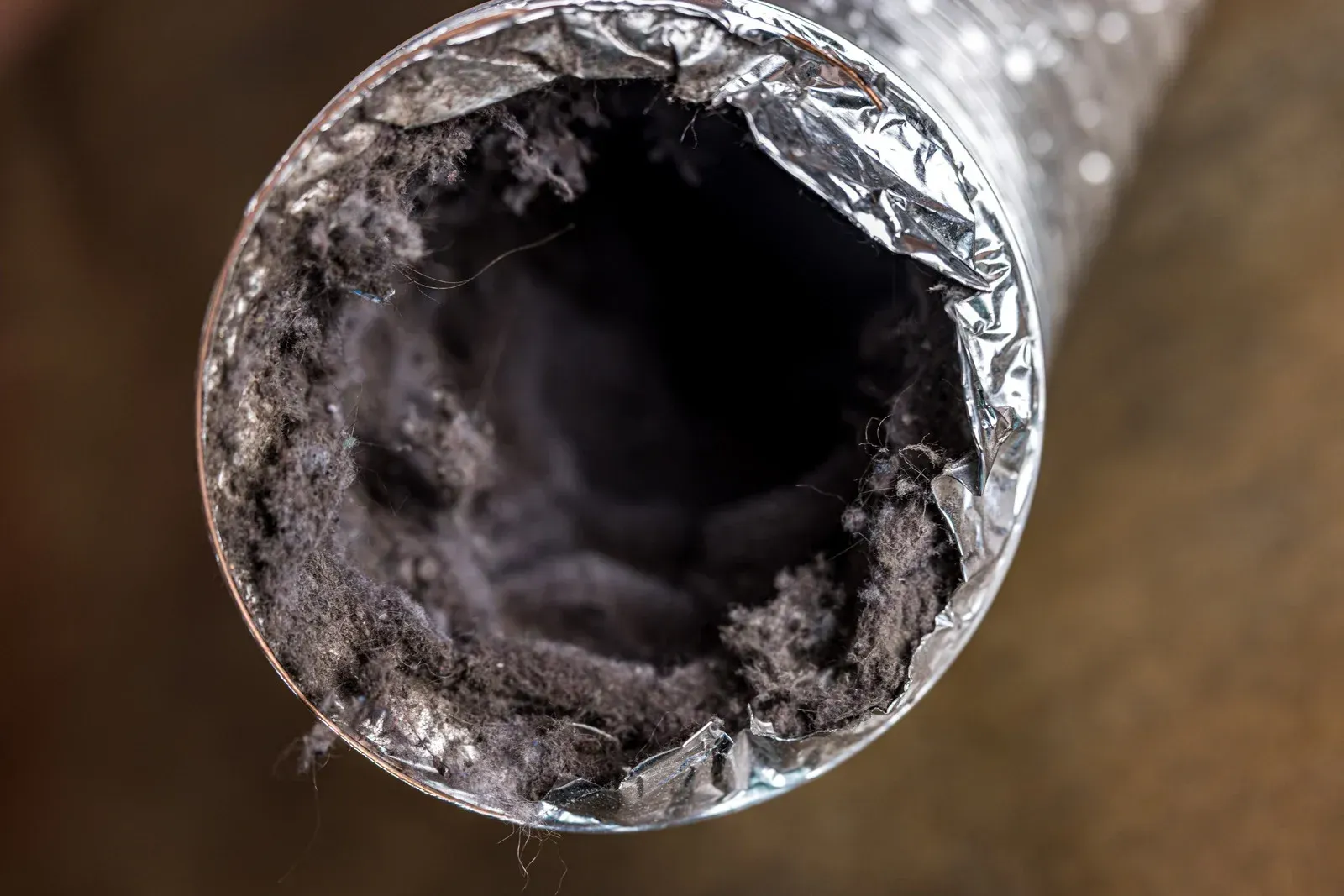 Inside of a dryer vent tube clogged with thick, dark gray lint buildup.