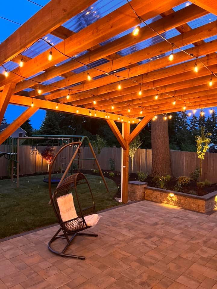 There is a rocking chair under a pergola with lights hanging from it.
