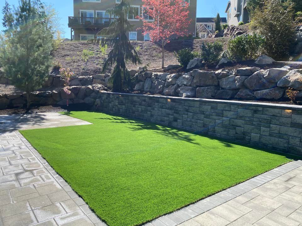 A large lawn with a stone wall in the background and a house in the background.
