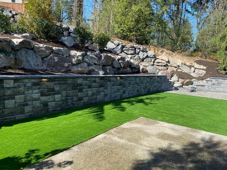 A stone wall surrounds a lush green lawn in a backyard.