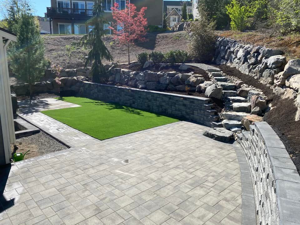 A backyard with a stone wall , stairs , and a grassy area.