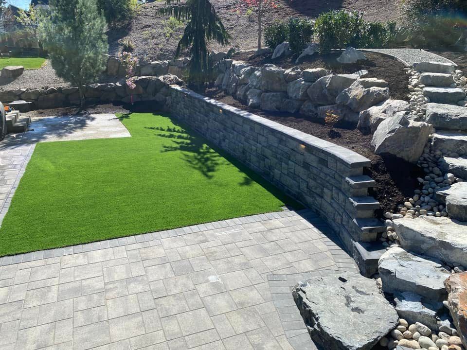 A patio with a stone wall , stairs , and a lush green lawn.