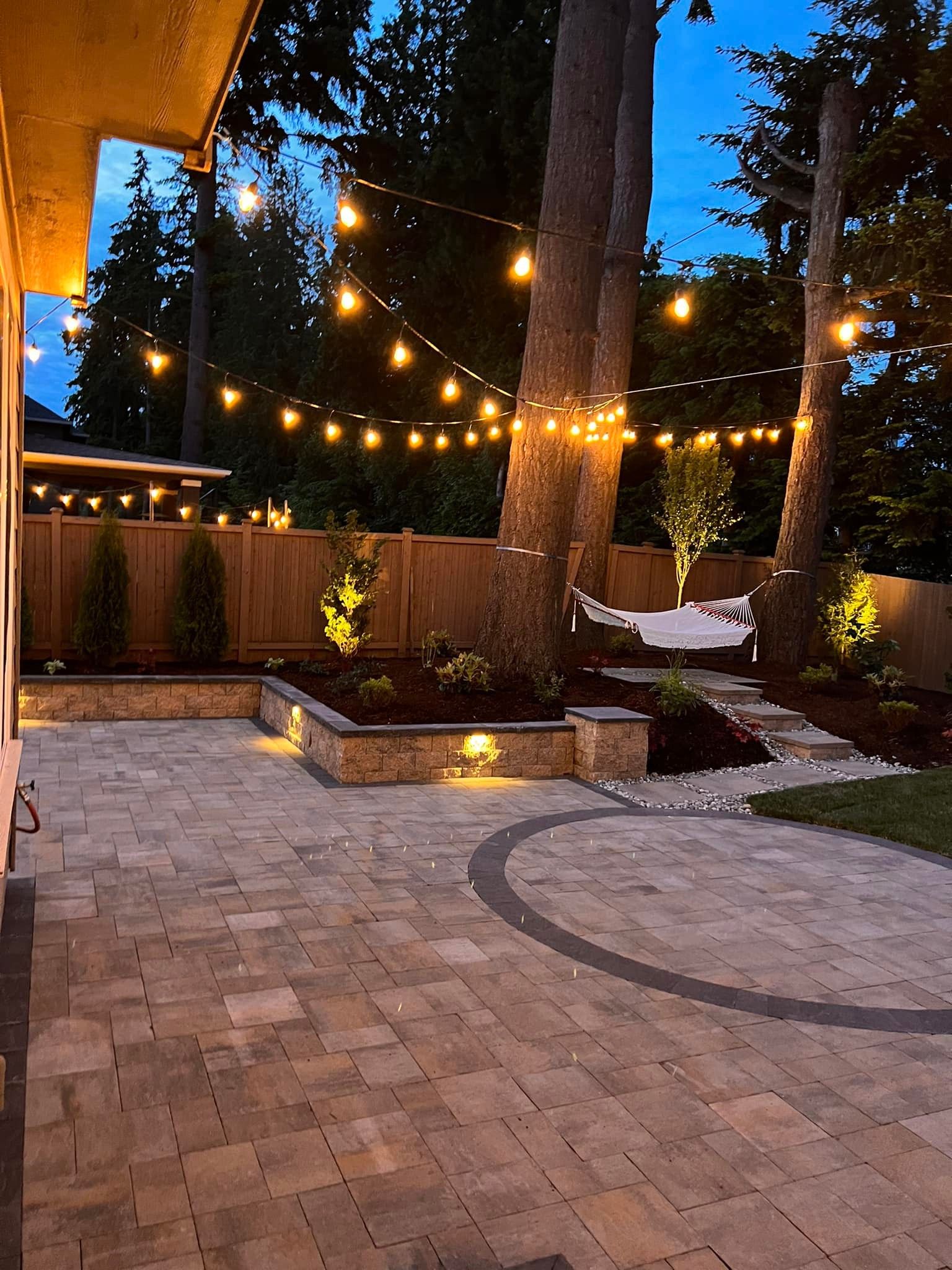 A backyard with a patio and trees covered in lights at night.