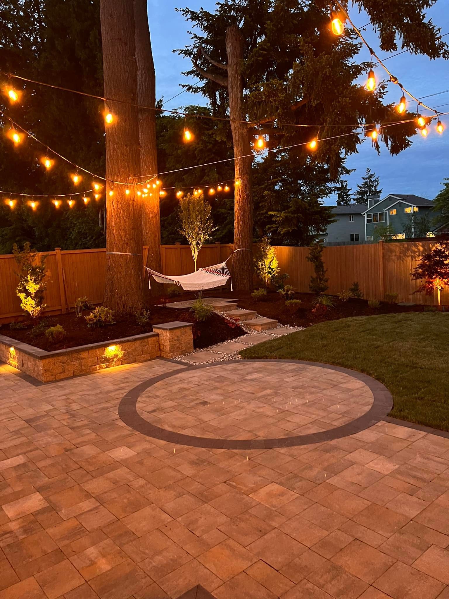 A patio with a hammock and lights hanging from the trees.