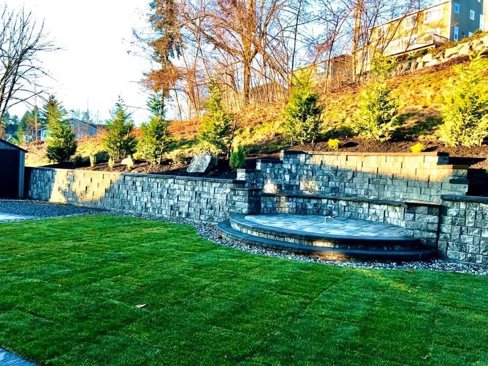 A backyard with a stone wall and a lush green lawn.