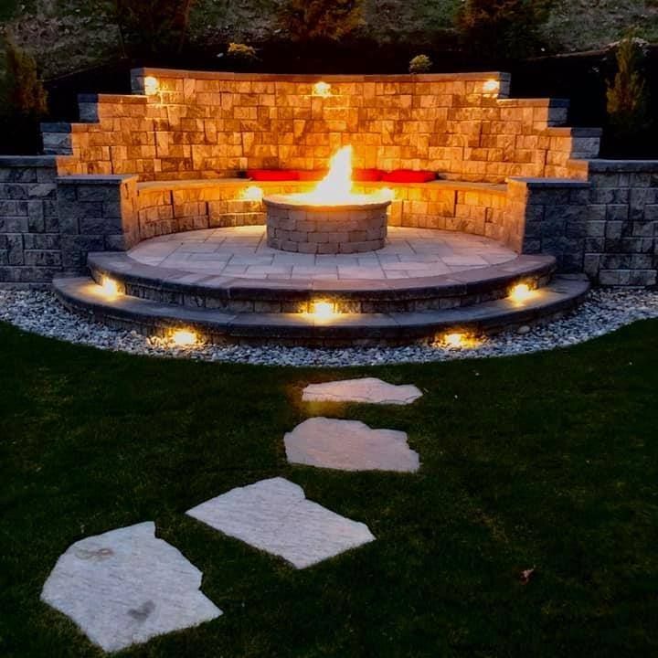 A fire pit is surrounded by a stone wall and lit up at night.