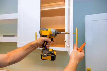 A man is using a drill to install a cabinet in a kitchen.