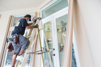 A man is standing on a ladder working on a window.