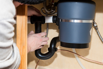 A person is fixing a garbage disposal under a sink.