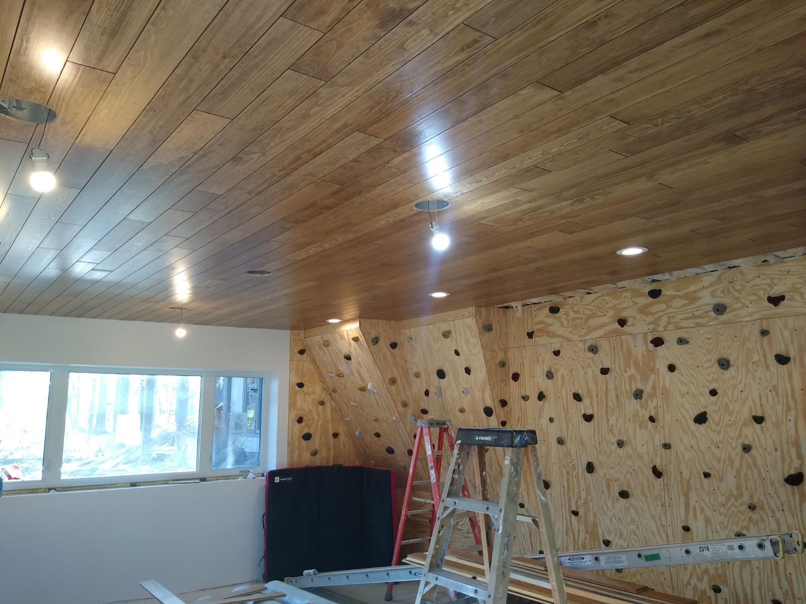 A room with a wooden ceiling and a climbing wall.