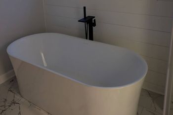 A white bathtub is sitting in a bathroom next to a black faucet.