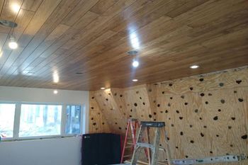 A room with a wooden ceiling and a climbing wall.
