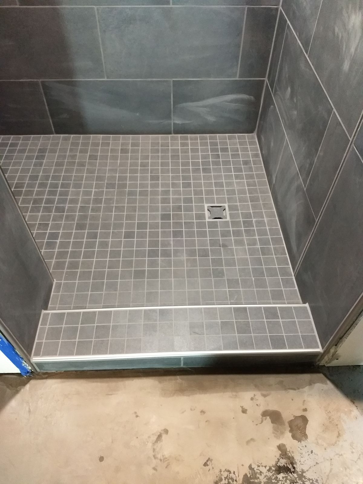 A shower stall with a tiled floor and a drain.