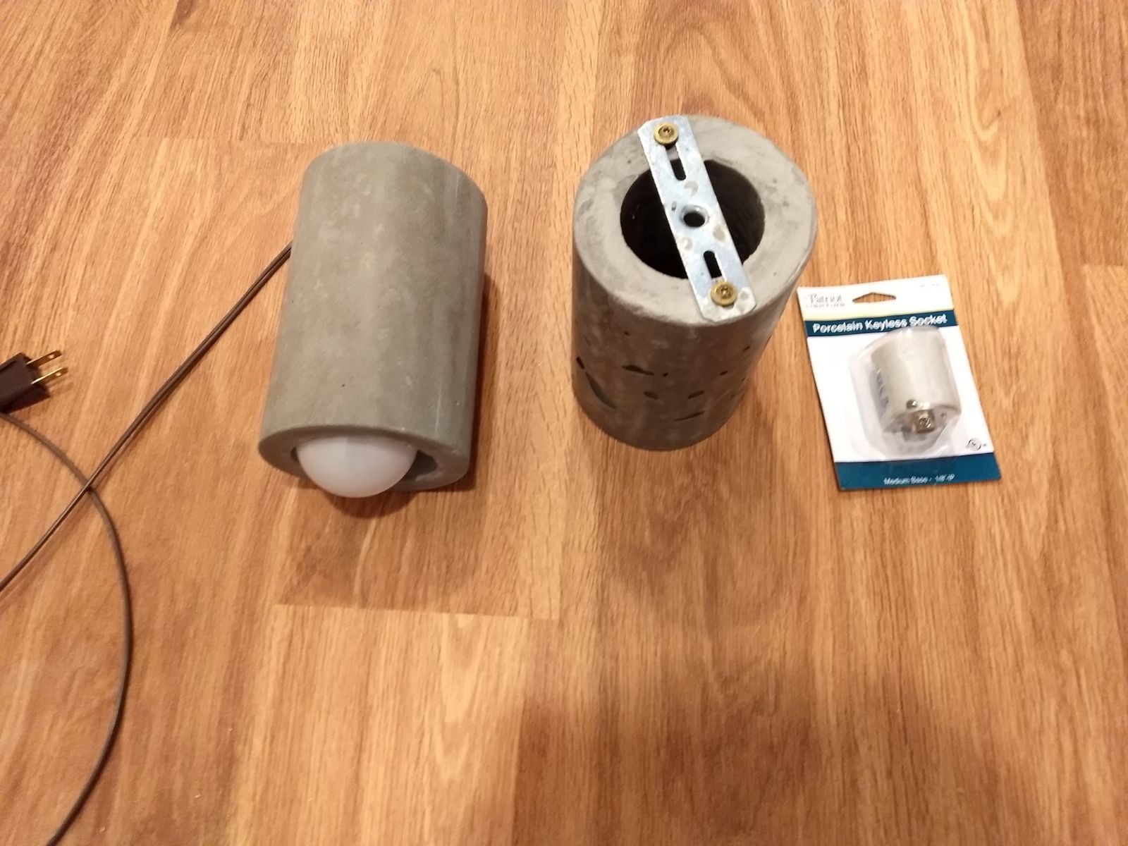 A pair of concrete cylinders sitting on a wooden floor next to a package of light bulbs