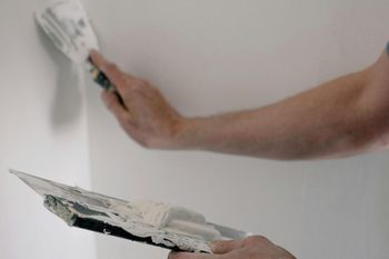 A person is plastering a wall with a trowel and brush.