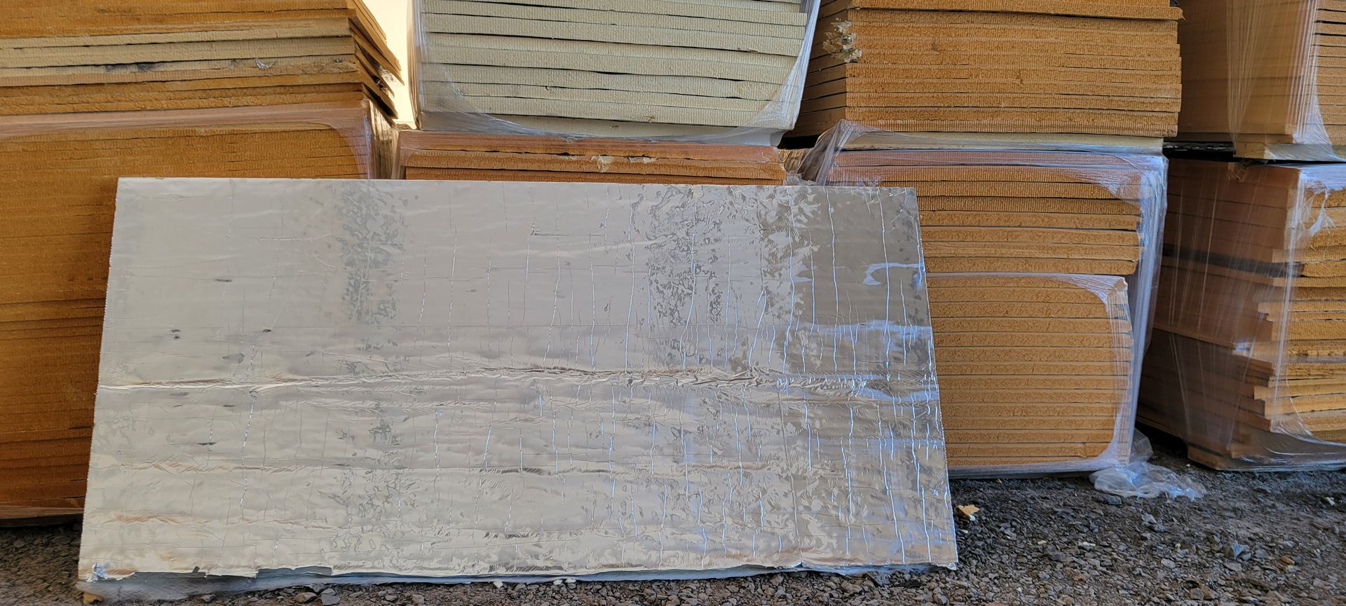 A reflective, silver-colored board in front of stacked wooden boards wrapped in plastic.