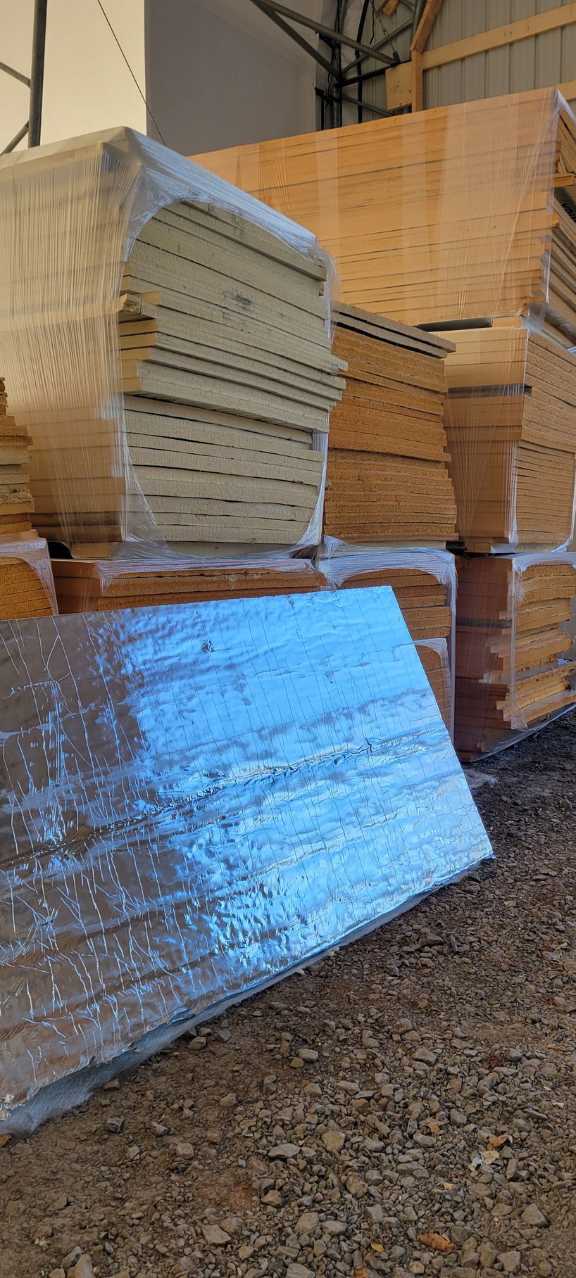 Stacks of wrapped construction materials in a warehouse. Various shades of brown and tan wood are visible.