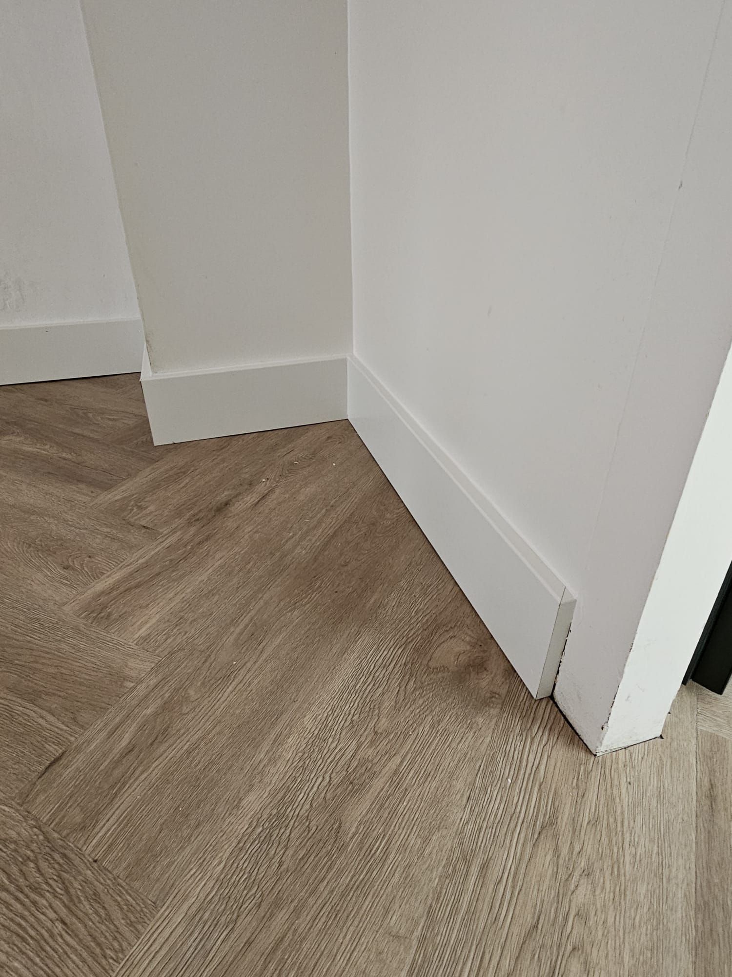Een hoek van een kamer met een houten vloer en witte muren.