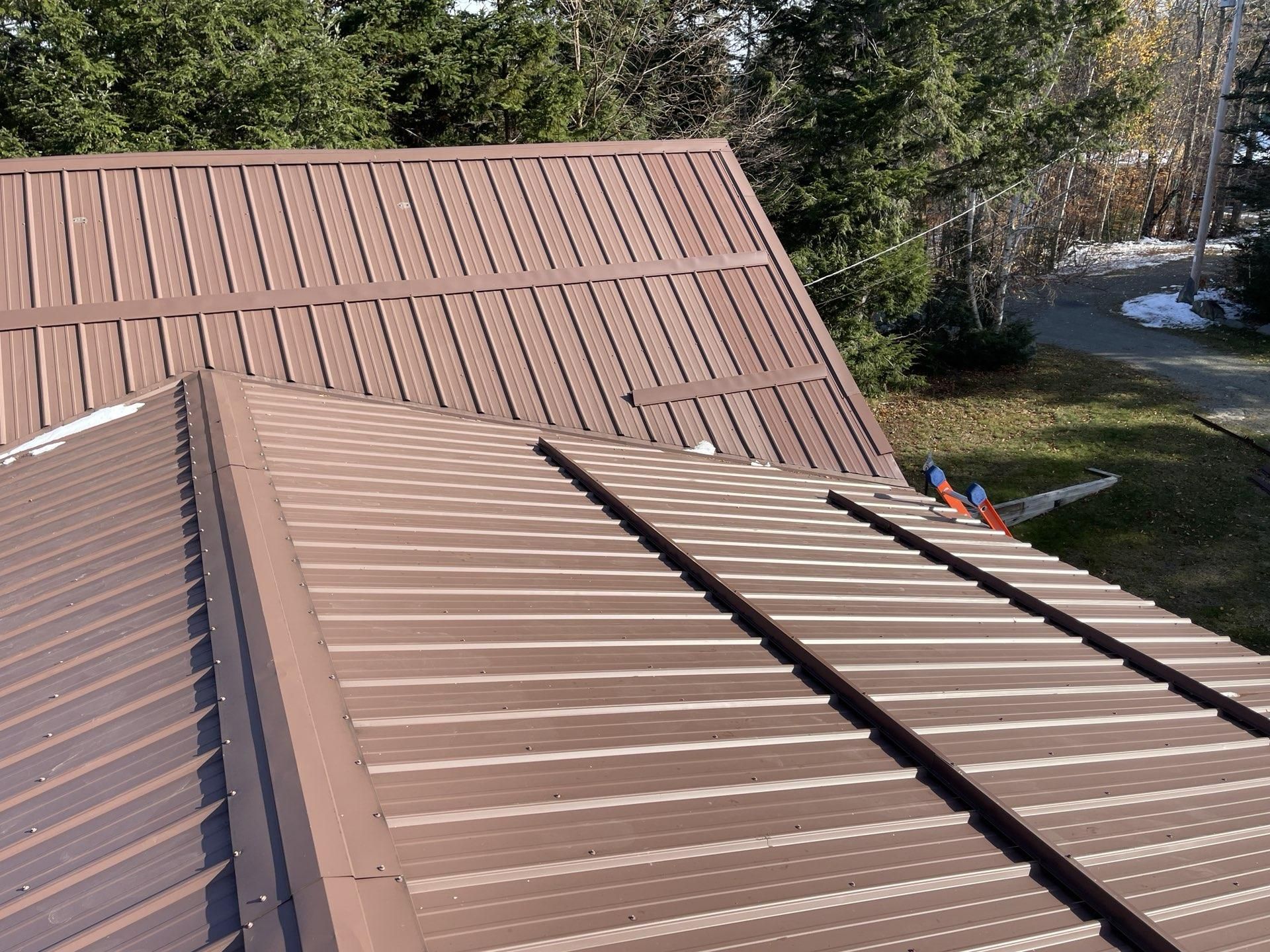 Brown metal roof with vertical ribbed panels, angled against a backdrop of trees.
