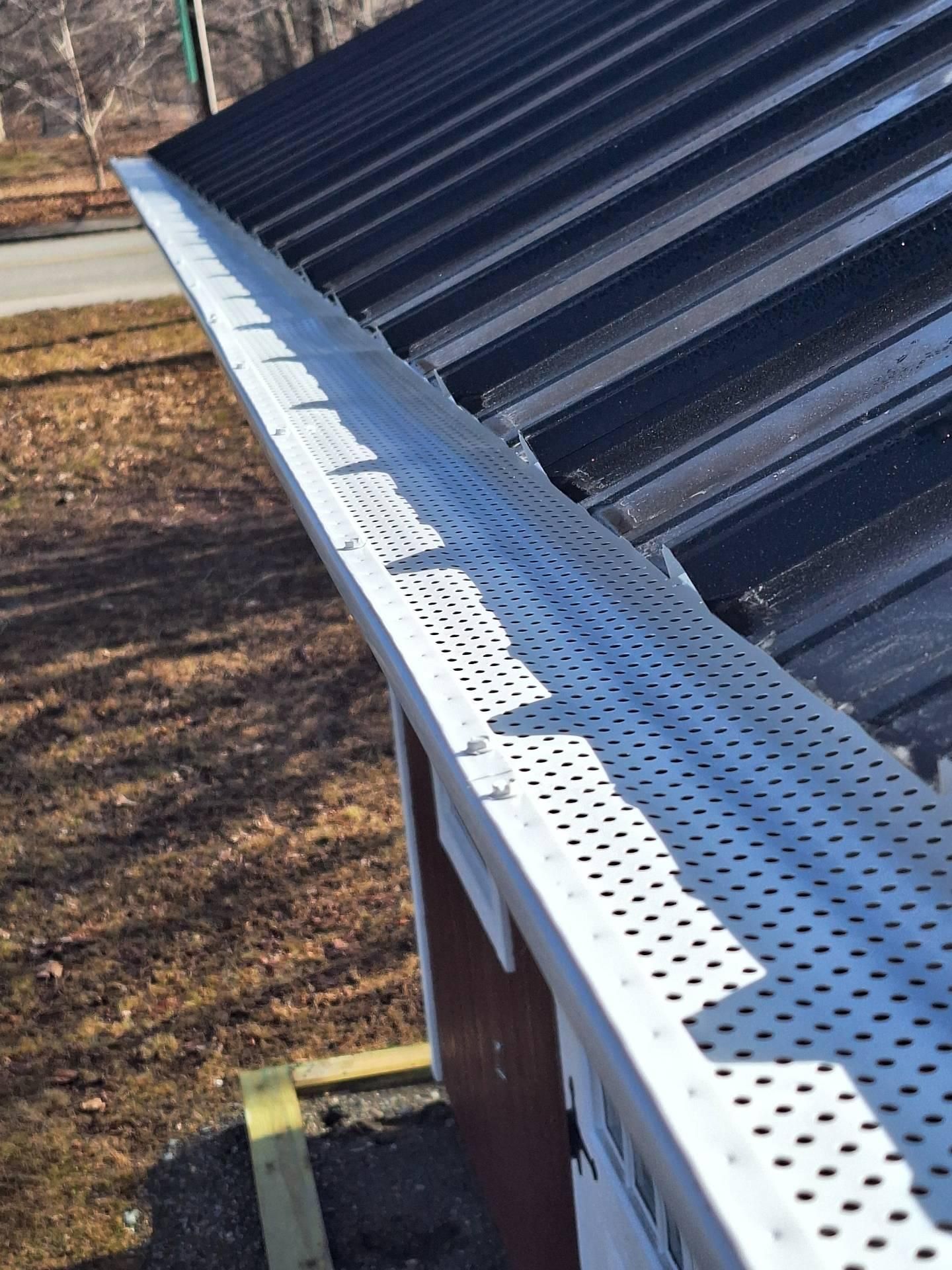 White gutter guard on a black metal roof, protecting the gutter from debris, outdoors.