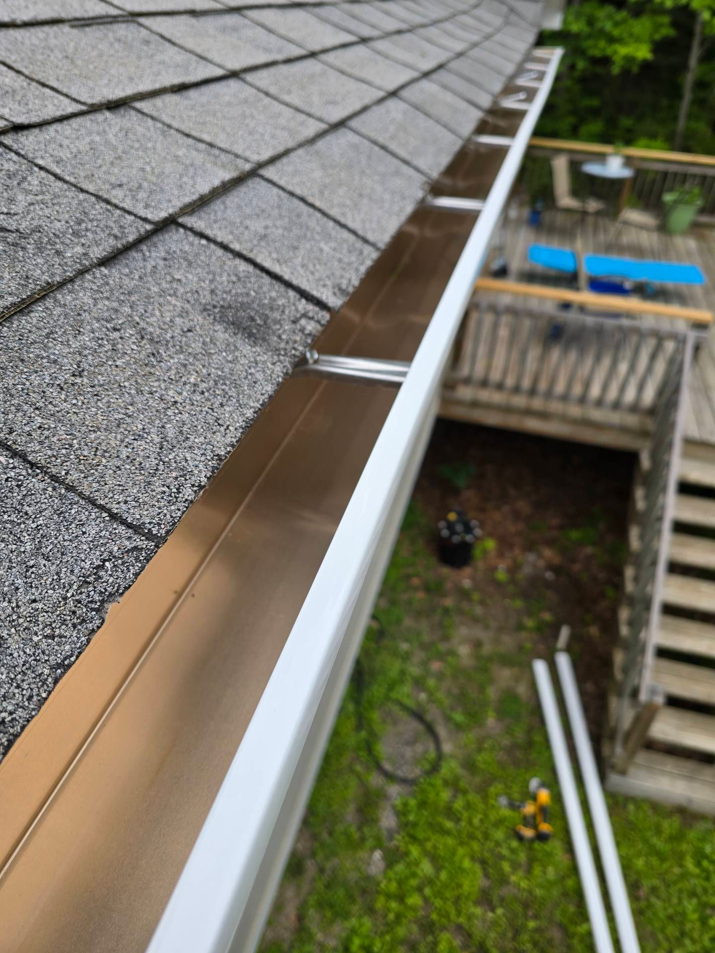 New copper-colored gutters installed along a shingled roof, with green grass and a wooden deck visible.