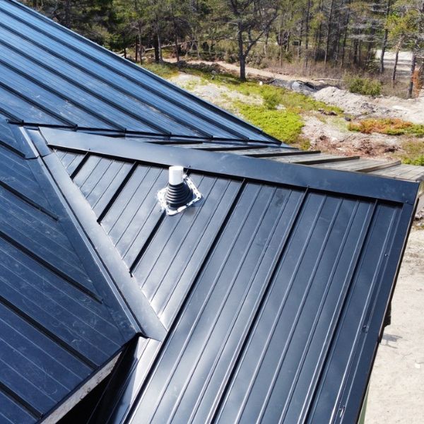 Black metal roof with a vent pipe, trees in the background.