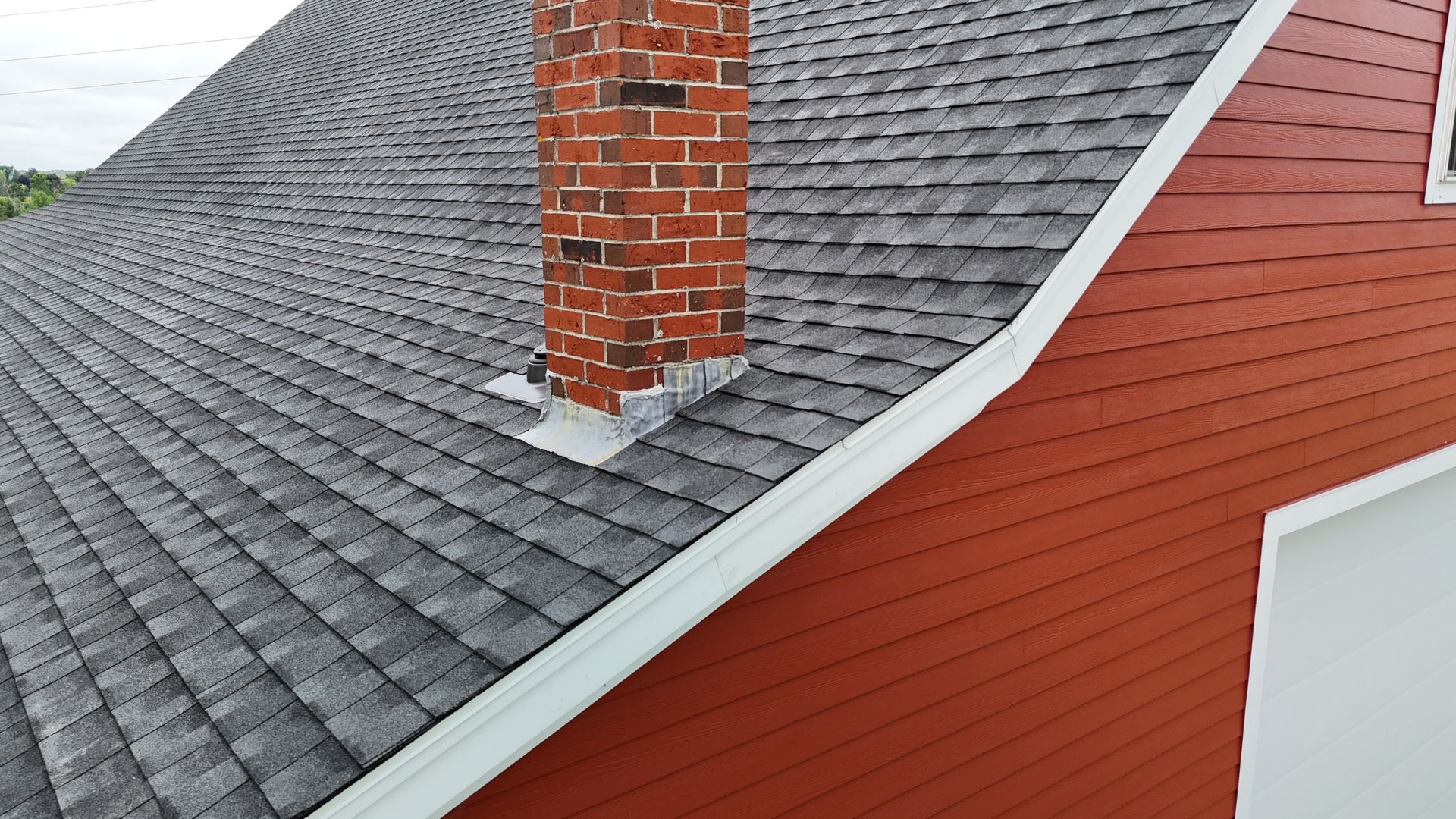 Red house with a brick chimney and gray shingled roof. White trim.