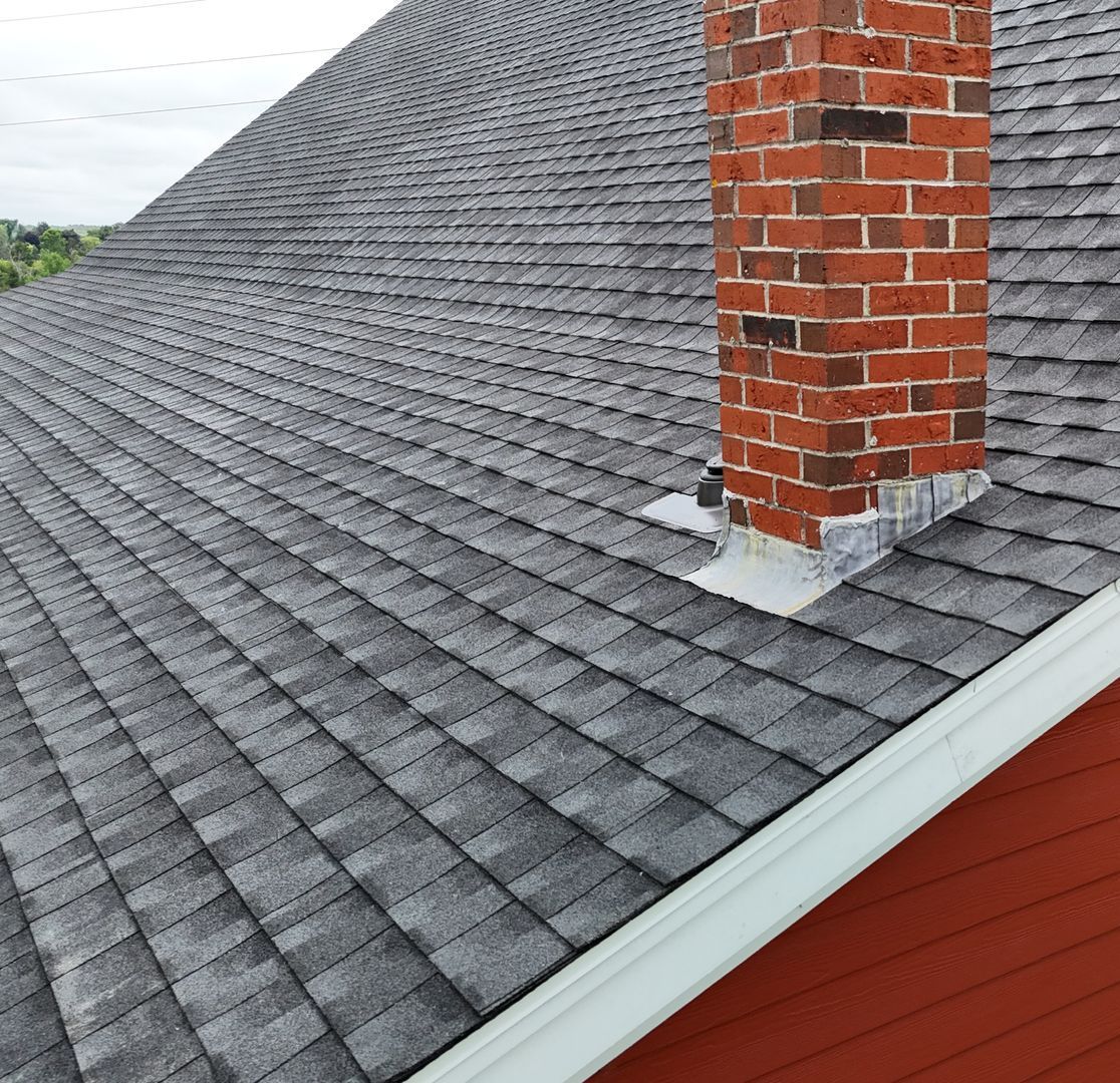 Gray shingle roof with red brick chimney and white trim on a red building.
