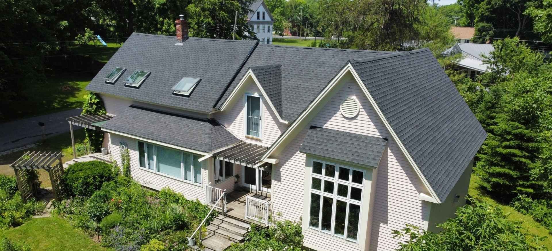 Pink house with a dark gray roof, surrounded by trees and greenery.