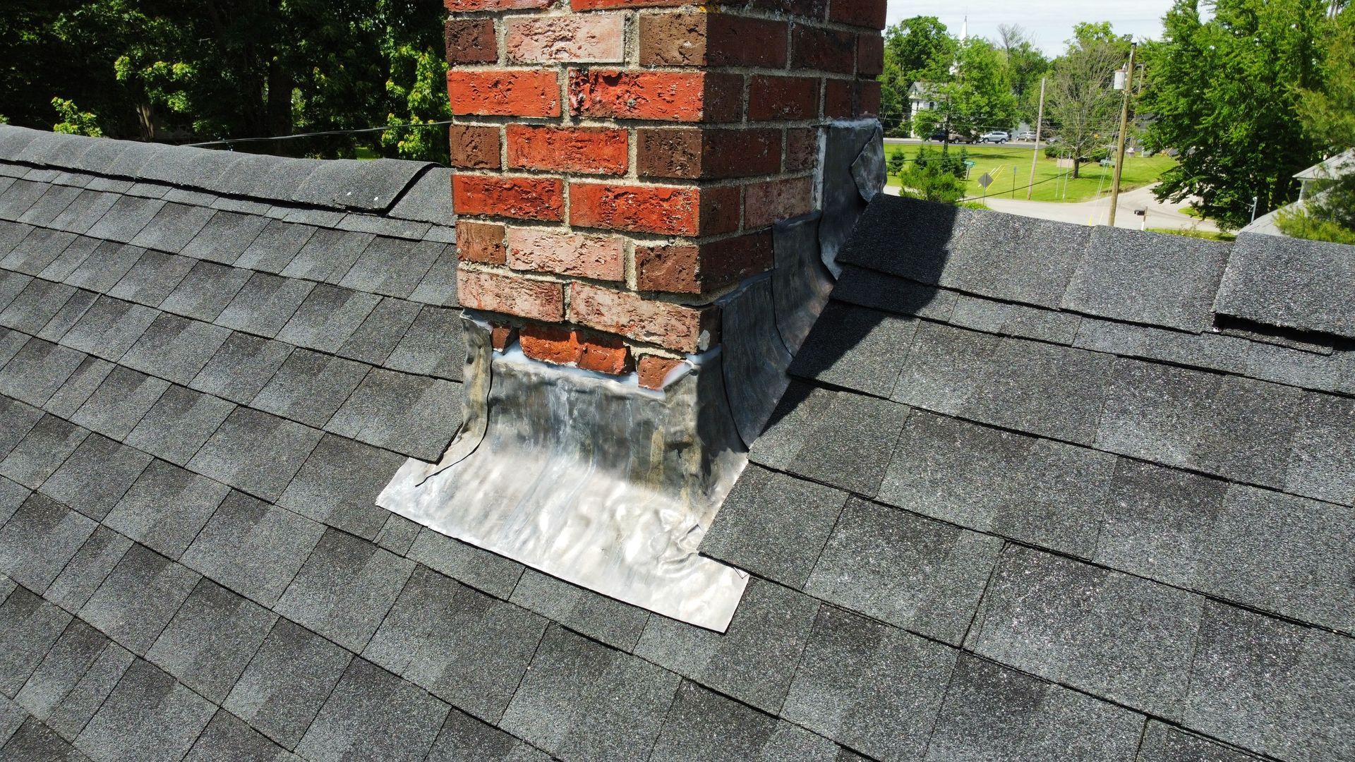 Brick chimney on a shingled roof, with flashing around the base; bright sunny day.