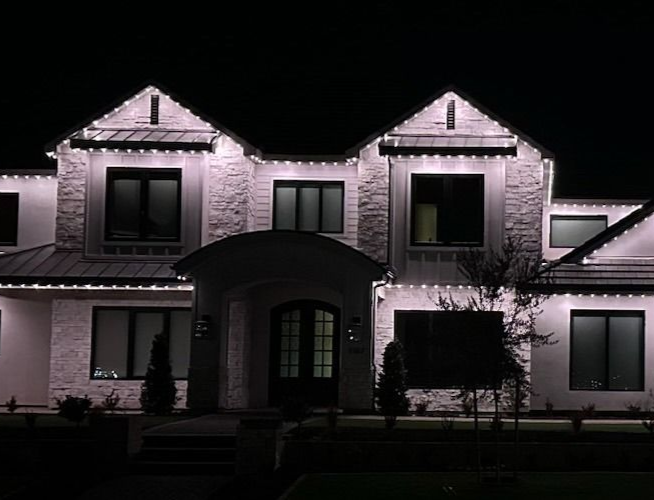 House exterior at night, lit up with white lights.