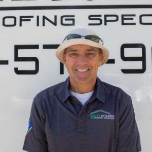 Man wearing hat, polo shirt, smiling in front of a business sign.