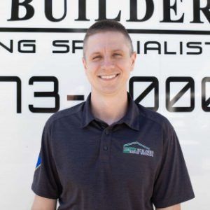 Man smiling in front of a sign for a builder, wearing a dark polo shirt.