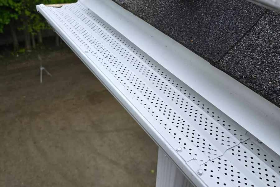 Silver gutter with perforated leaf guard attached to a dark roof.