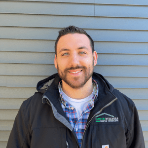 Man in black jacket smiling, standing in front of gray siding.
