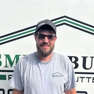 Man wearing glasses and a cap, in front of a sign with a building image and text.