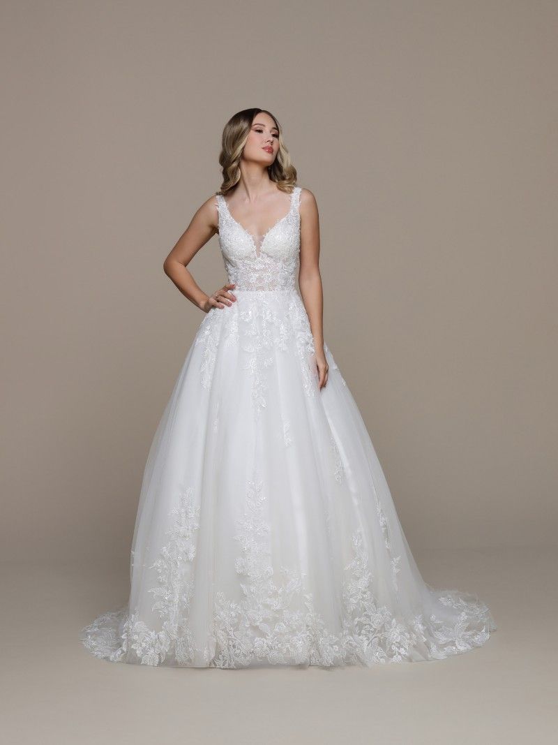 Woman in a white wedding gown with floral embroidery, posing with hand on hip.