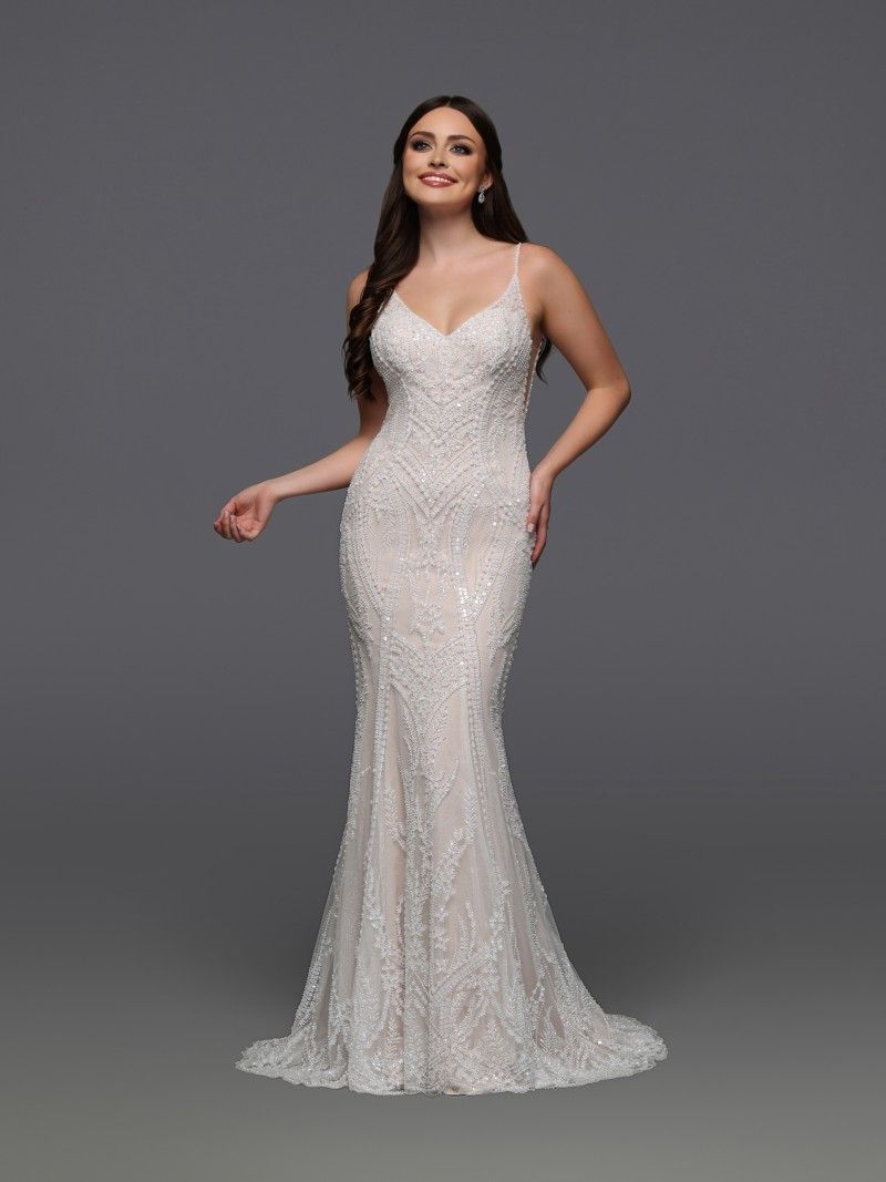 Woman in a beaded mermaid wedding dress smiles, standing against a grey backdrop.