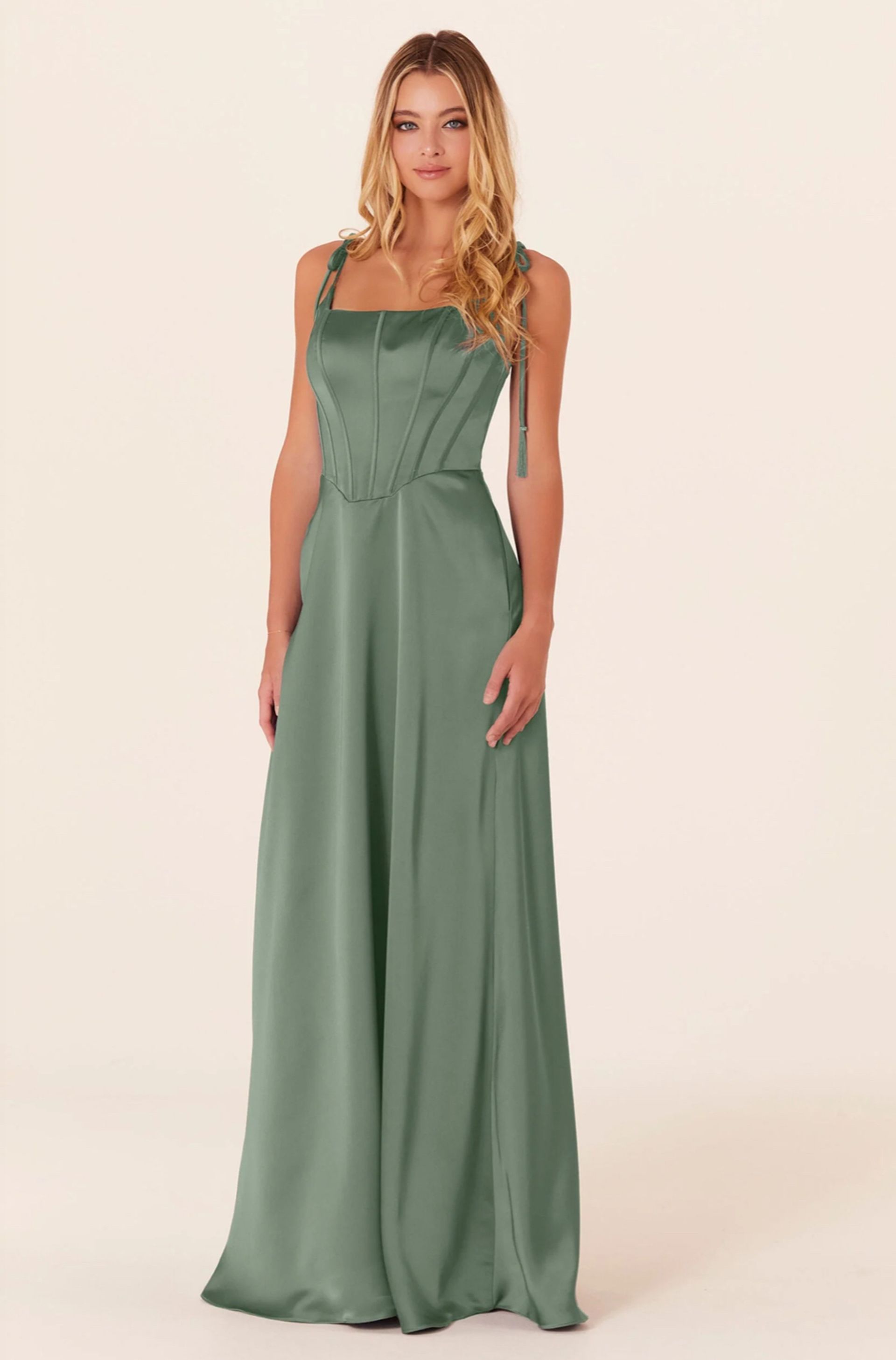 Woman in a sage green formal dress with a square neckline, standing in a studio.