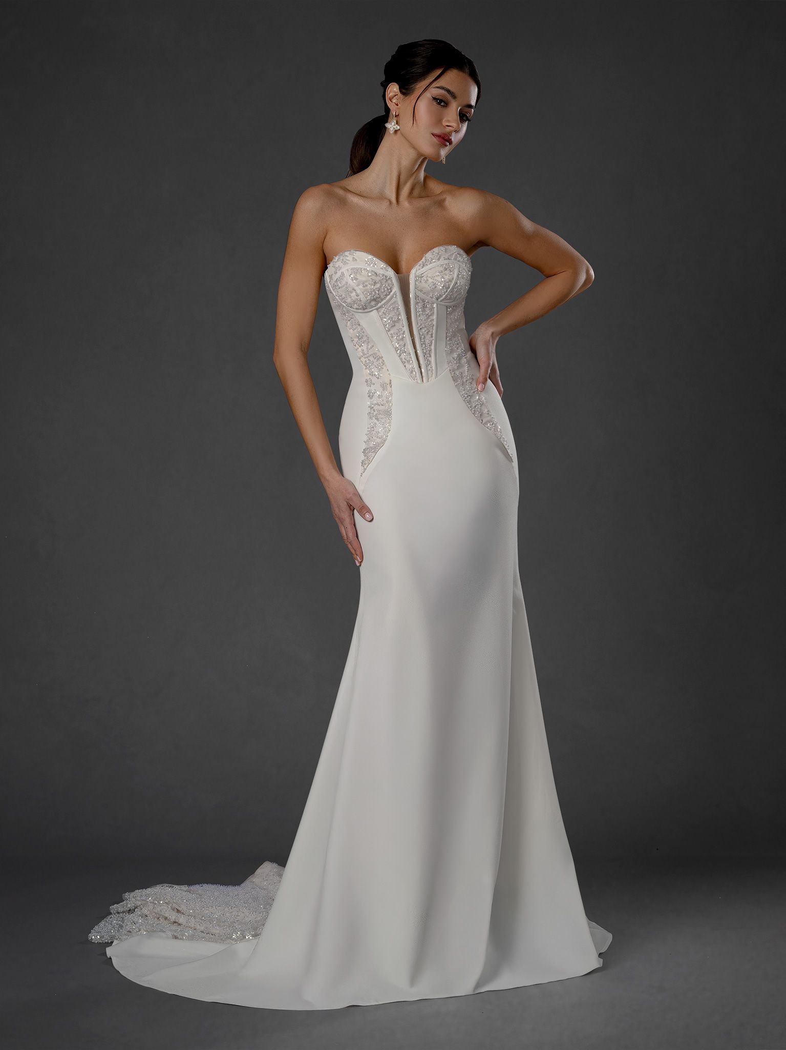 Woman in strapless white wedding dress, embellished bodice, mermaid skirt, on gray background.