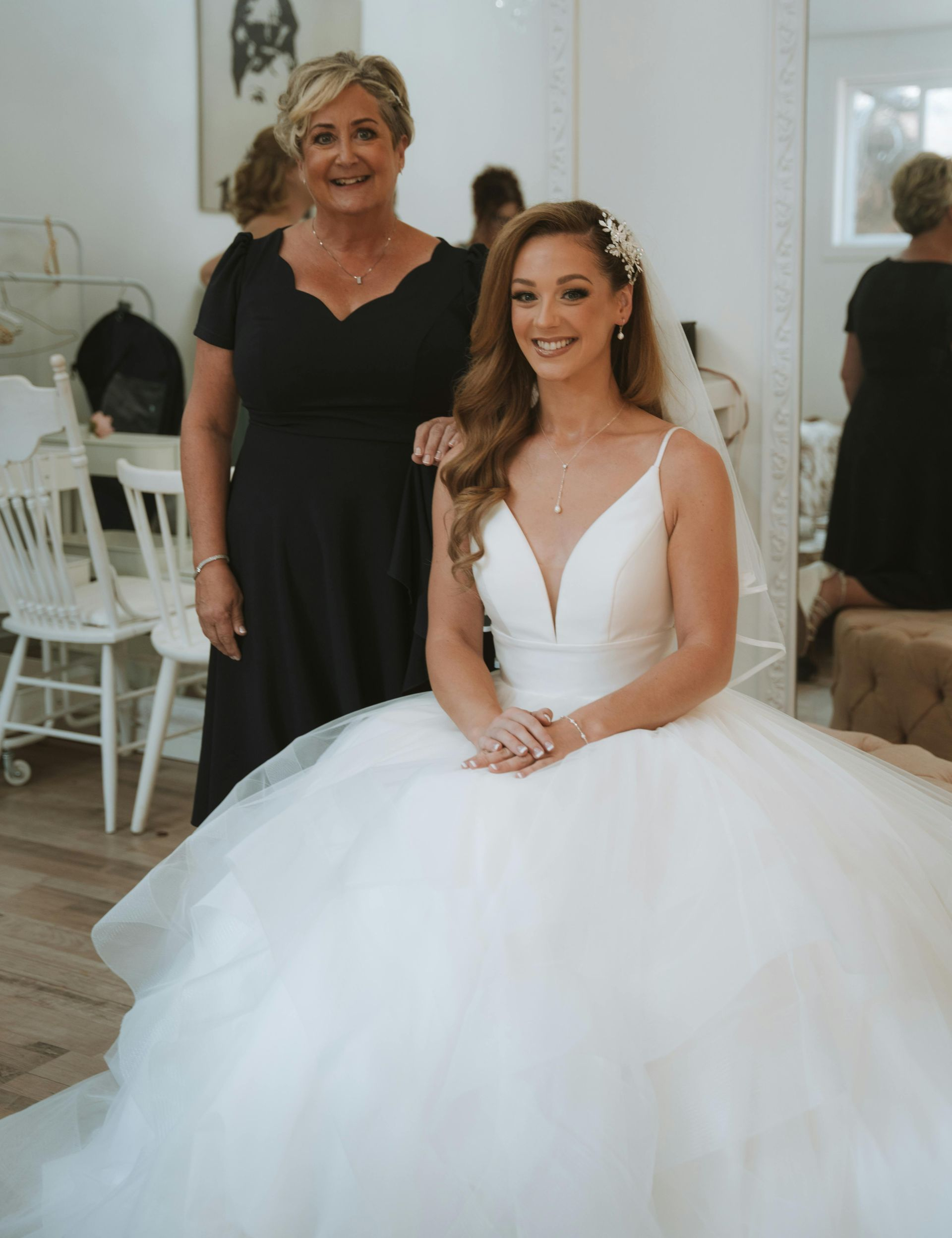 Bride in white wedding dress with mother in black dress in a bright room with mirrors.