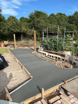 A concrete walkway is being built in a backyard with trees in the background.