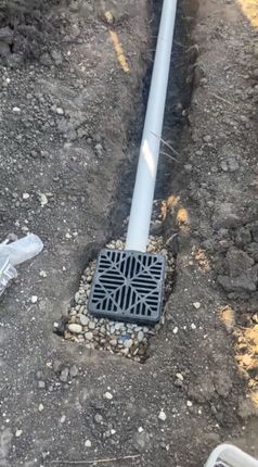 A white pipe is sitting in the dirt next to a drain.
