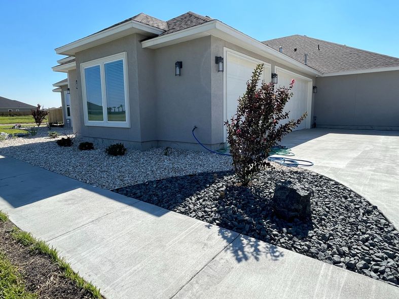 A house with a concrete driveway and a bush in front of it.