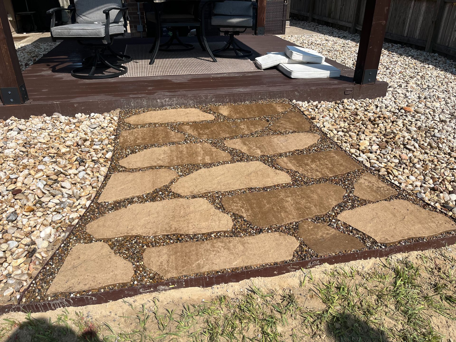 A stone walkway leading to a patio with a table and chairs under a pergola.